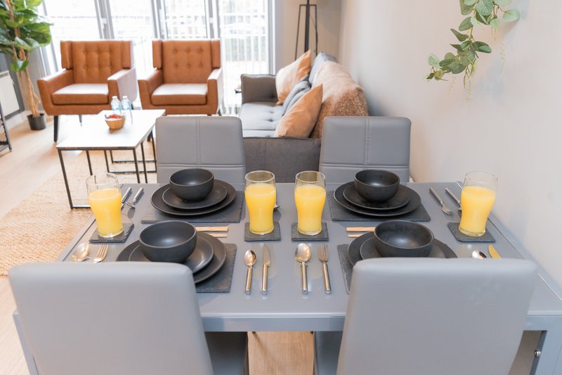 Dining table set for two with black plates, candles, and grey chairs, lounge visible beyond