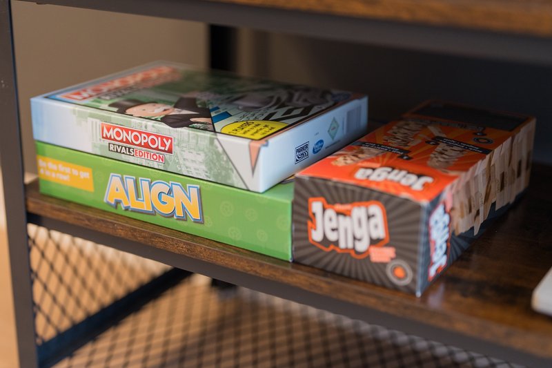 Wooden shelf with stacked board games including Monopoly, Align, and Jenga