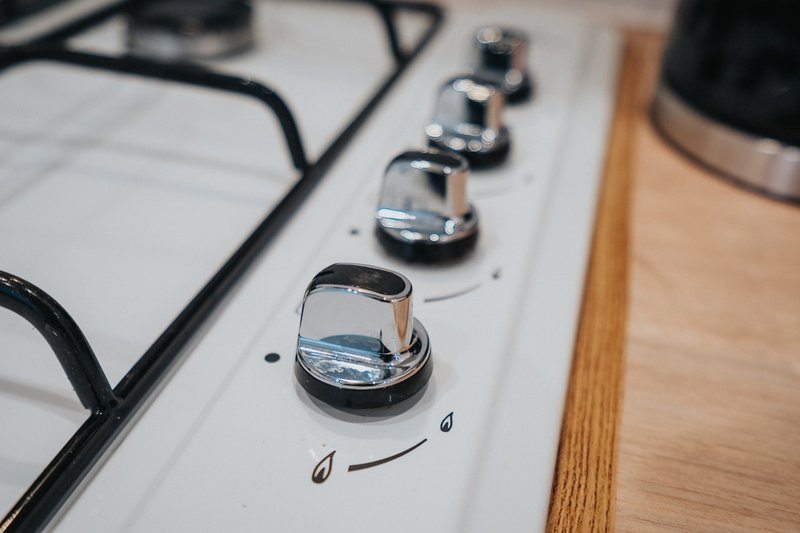 Close-up of kitchen stovetop control knobs with black power cables and wooden countertop