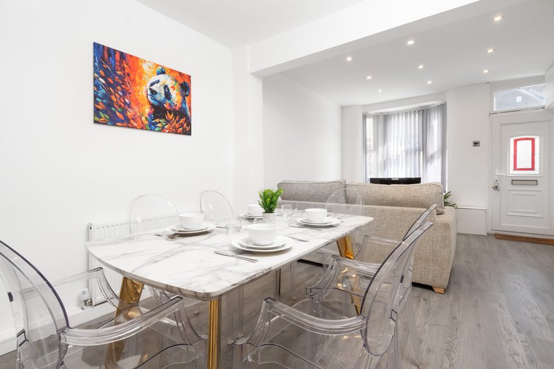 Open-plan living area with dining table, transparent chairs, sofa, and wall art