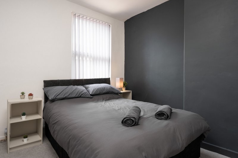 Modern bedroom with double bed, dark headboard, dark accent wall and vertical blinds