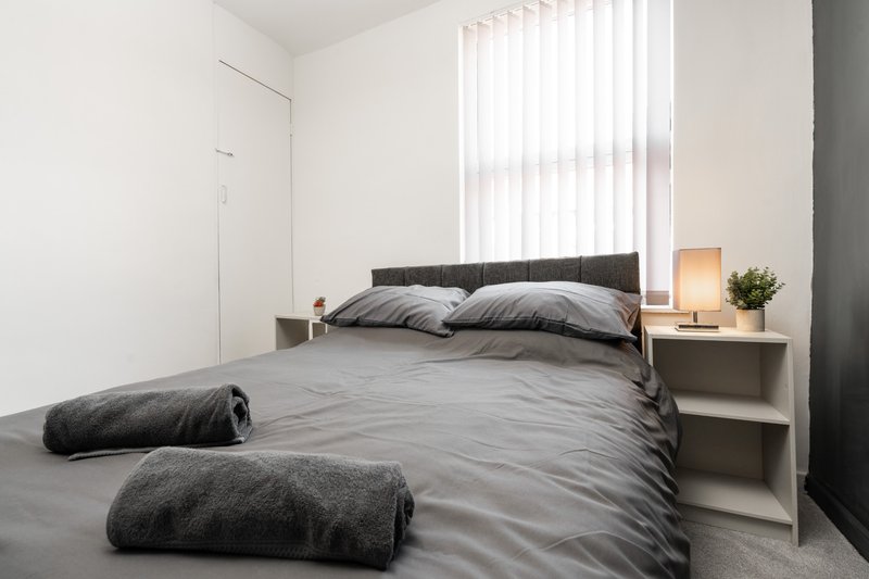 Modern minimalist bedroom with double bed, grey bedding, nightstand and vertical blinds