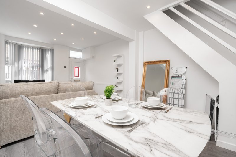 Modern open-plan kitchen and dining area with marble island, white place settings, and beige sofa