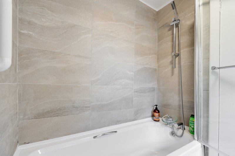 Modern bathroom with white bathtub, grey tile walls, and shower enclosure