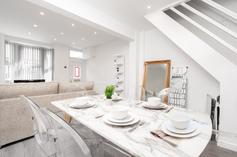 Modern open-plan dining and living area with marble table, place settings, and neutral furnishings