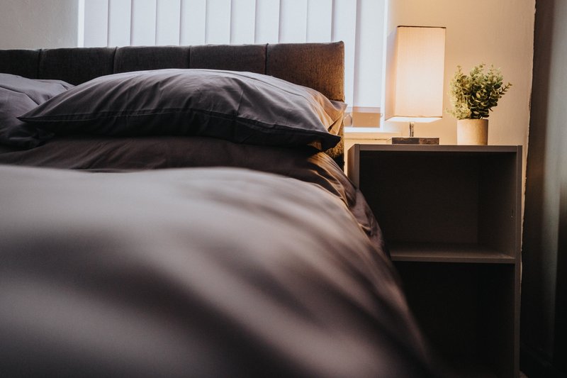 Modern bedroom with dark bedding, wooden headboard, and minimalist nightstand with lamp