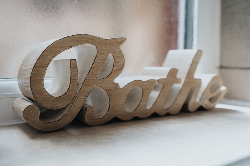 Wooden decorative sign reading 'Breathe' on white windowsill with blurred background