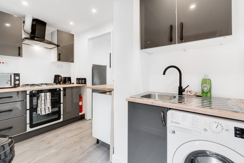 Modern kitchen with black and grey cabinetry, gas hob, washing machine and stainless steel sink