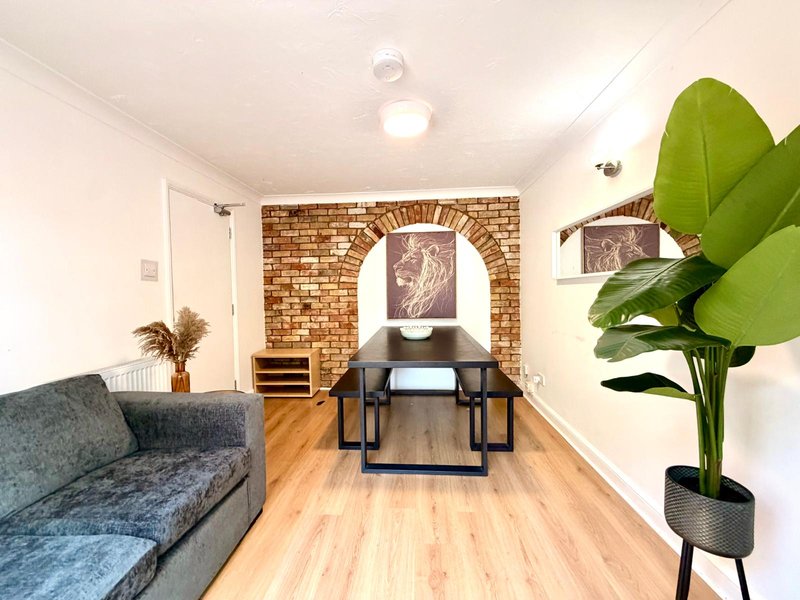 Open-plan living space with sofa, dining table, exposed brick wall and potted plant