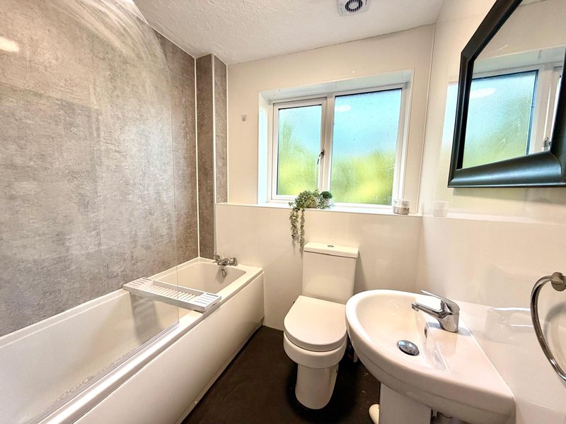Modern bathroom with bathtub, toilet, sink, mirror and bright window overlooking garden