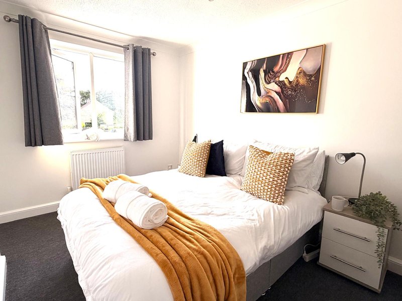 Bright bedroom with double bed, white bedding, gold throw, patterned cushions and window
