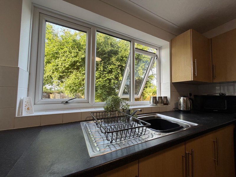 Kitchen with wooden cabinets, black countertop, sink with dish rack, and large window overlooking garden