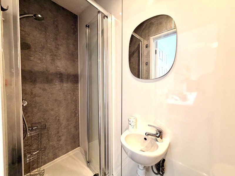 Compact bathroom with shower enclosure, wall-mounted sink, oval mirror and cream walls