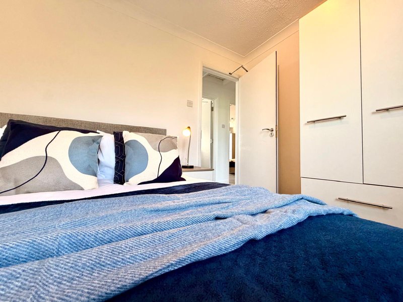 Modern bedroom with double bed, blue bedding, geometric cushions, and white built-in wardrobe