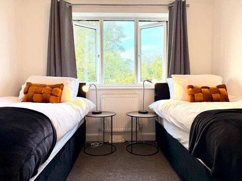 Bright twin bedroom with two beds, orange cushions, large windows and grey curtains