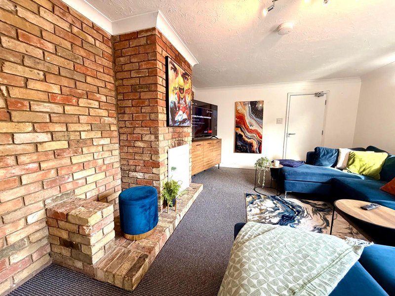 Modern living room with exposed brick fireplace, blue seating, and wall art