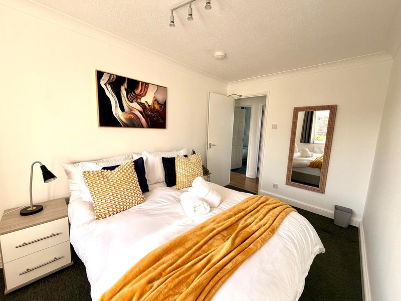 Modern bedroom with double bed, gold throw, patterned cushions, bedside lamp and wall art