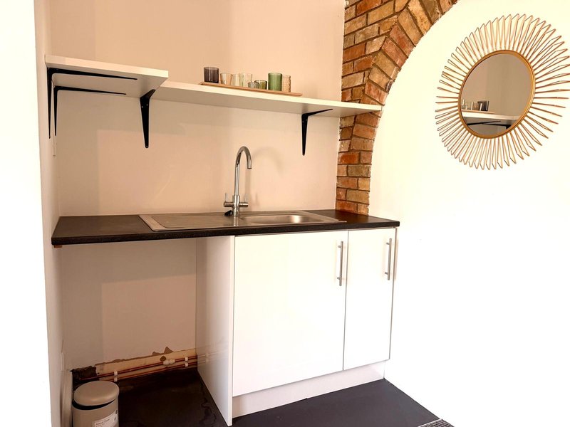 Compact kitchenette with white cabinetry, black countertop, sink, exposed brick wall and decorative mirror