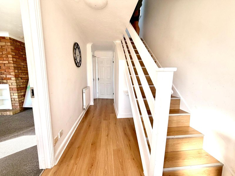 Hallway with wooden flooring, white walls, stairs with brown treads, and wall clock