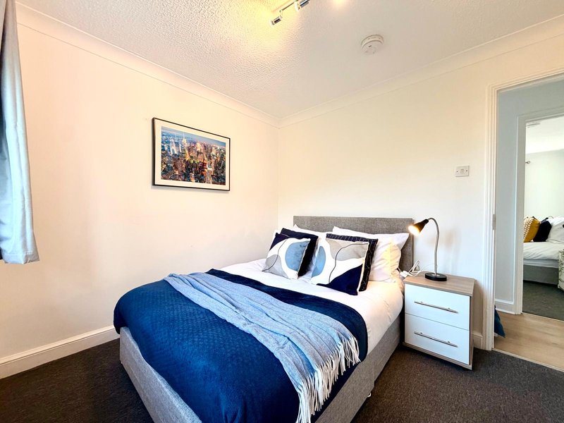 Bedroom with double bed, blue bedding, white nightstand and framed wall art