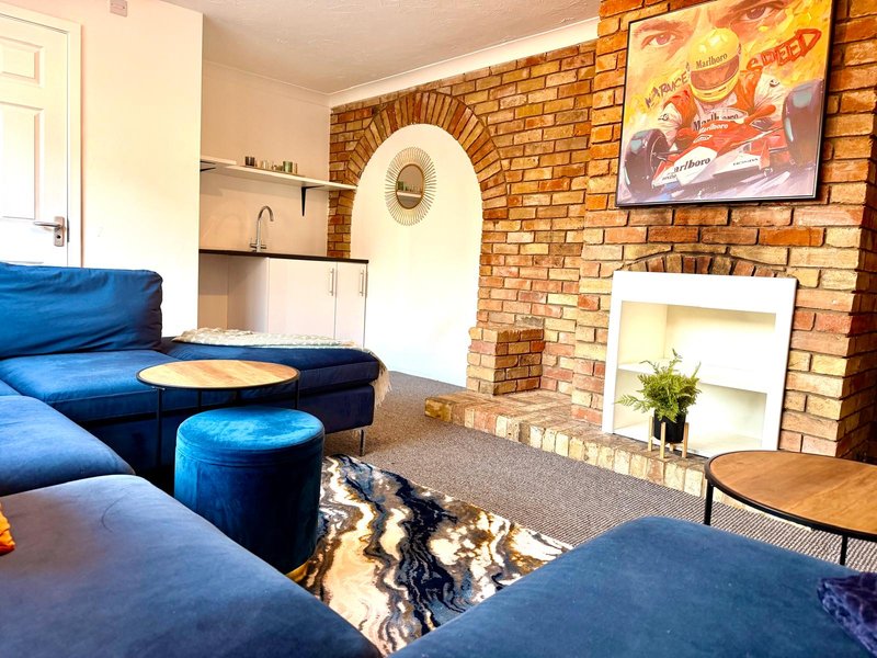 Living room with blue velvet sofa, exposed brick fireplace, white shelving and wooden furniture
