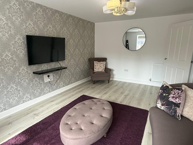 Modern living room with wall-mounted TV, patterned wallpaper, purple ottoman and rug