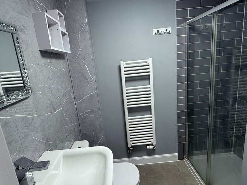 Modern bathroom with grey tile walls, white toilet, towel radiator, and walk-in shower enclosure