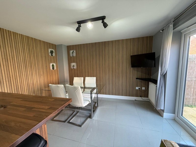 Modern living area with dining table, white chairs, wall-mounted TV, and patio doors
