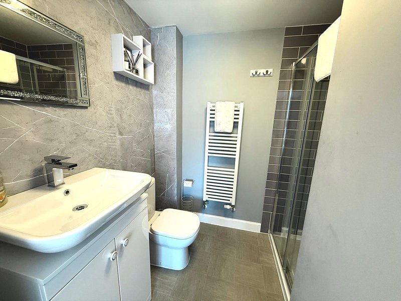 Modern bathroom with white sink vanity, toilet, heated towel rail and shower enclosure
