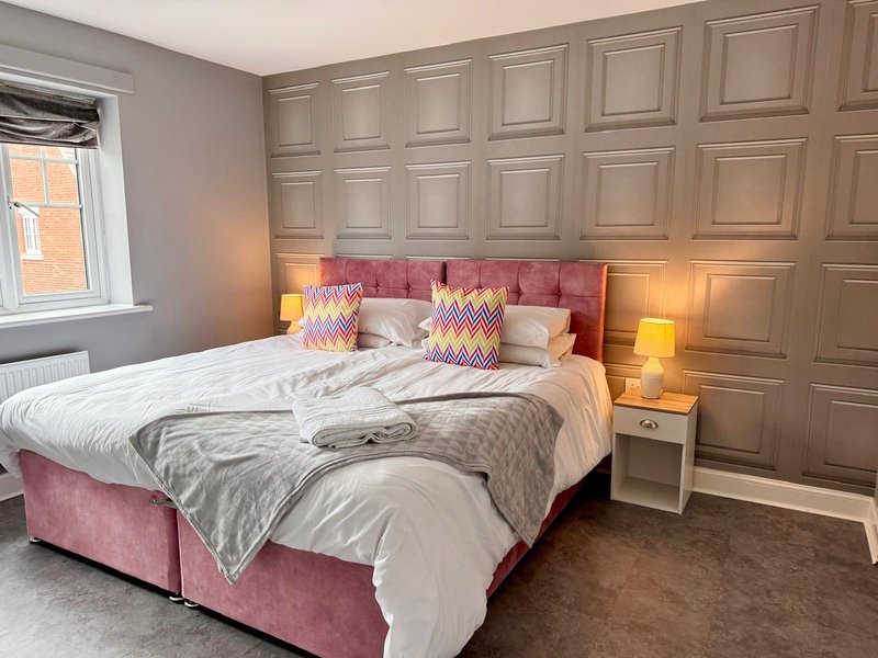 Modern bedroom with pink upholstered bed, panelled feature wall, bedside lamps and window