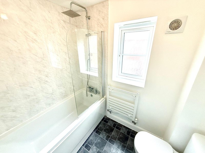 Modern bathroom with bathtub, glass shower screen, toilet, heated towel rail and window