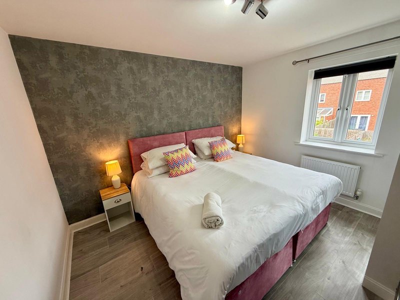 Modern bedroom with double bed, pink headboard, bedside lamps and feature wall