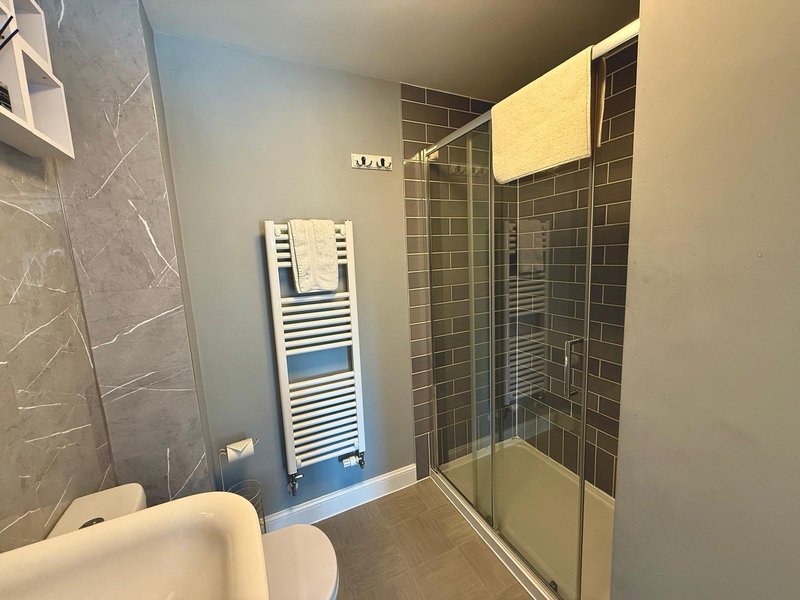 Modern bathroom with toilet, towel rail, shower enclosure and dark tile walls