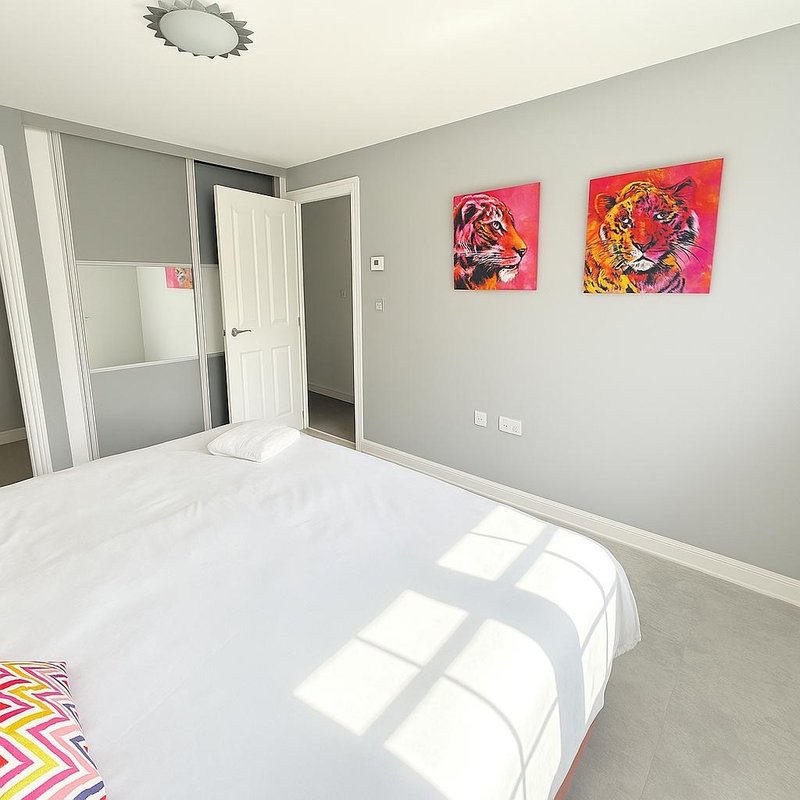 Modern bedroom with white bed, gray walls, colorful wall art, and ensuite door