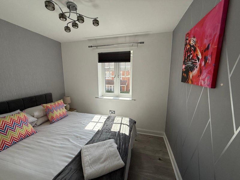 Modern bedroom with double bed, colorful pillows, grey walls and ceiling light fixture