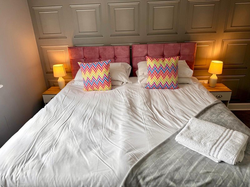 Modern bedroom with pink upholstered headboard, white bedding, patterned cushions and side lamps
