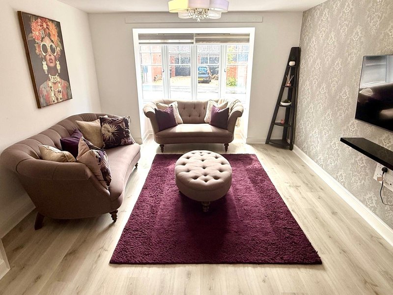 Modern living room with brown sofas, purple rug, cream ottoman and large window
