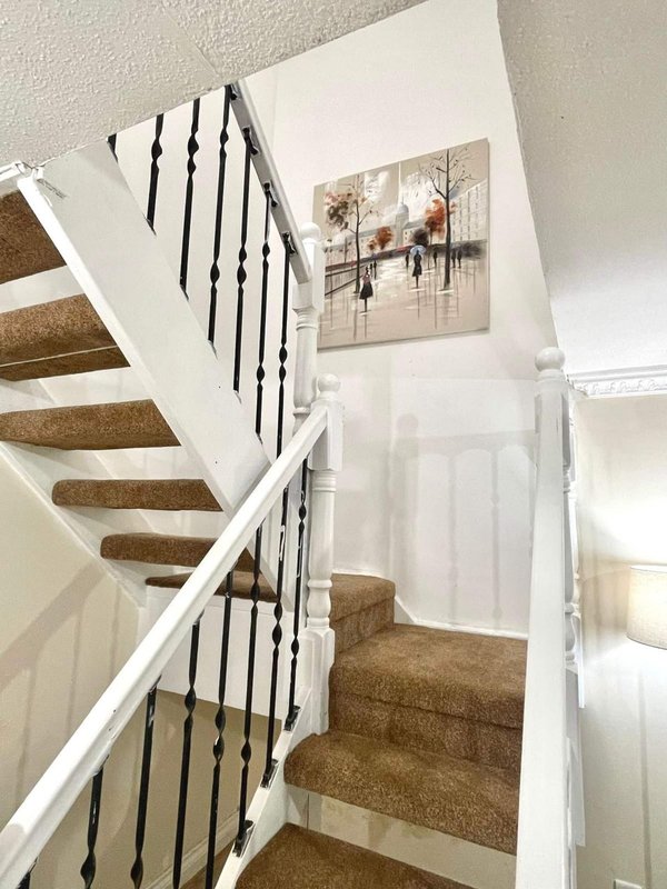 Staircase with white walls, black metal railings, and brown carpet runner