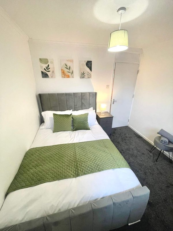 Compact bedroom with grey upholstered headboard, green bedding, pendant light and wall art