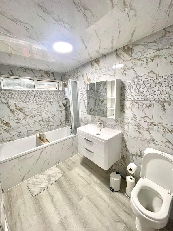 Modern bathroom with marble-look tiling, white vanity, mirror, bathtub and toilet