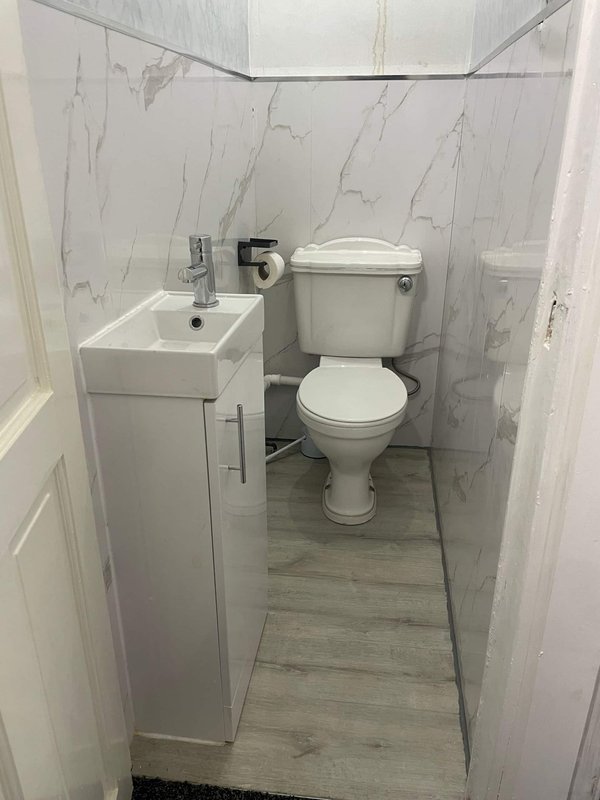 Modern bathroom with white toilet, wall-mounted sink, marble-effect tiles and wooden-look flooring