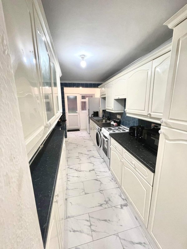 Modern galley kitchen with white cabinetry, black countertops, marble flooring and integrated appliances
