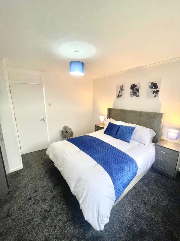 Modern bedroom with double bed, blue throw, white bedding, grey headboard, nightstands, and wall art