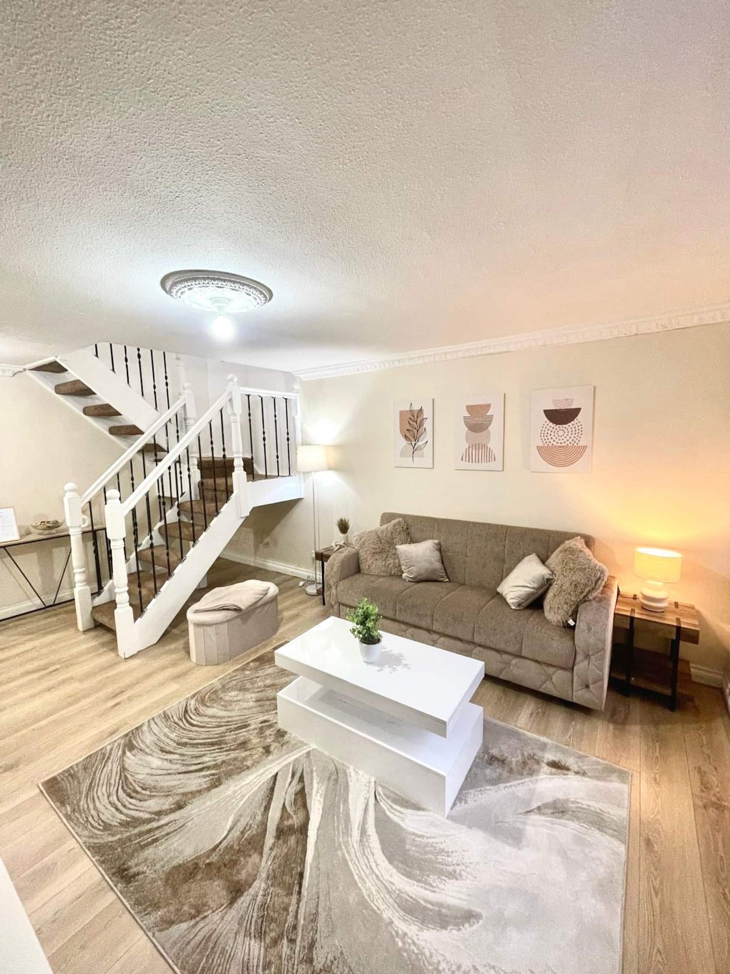 Modern living room with staircase, grey sofa, white coffee table and wooden flooring