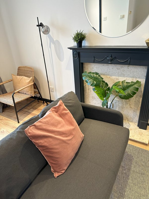 Living room with dark sofa, coral cushion, fireplace with plants, round mirror and floor lamp