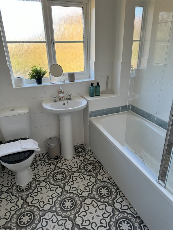 Clean bathroom with pedestal sink, toilet, bathtub, patterned floor tiles and window