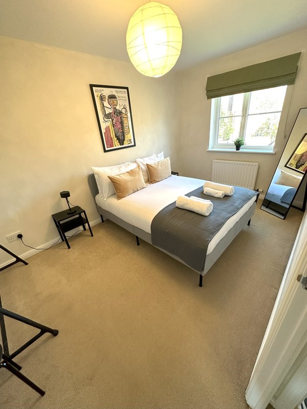 Bright bedroom with double bed, round ceiling light, framed artwork and window with green blind