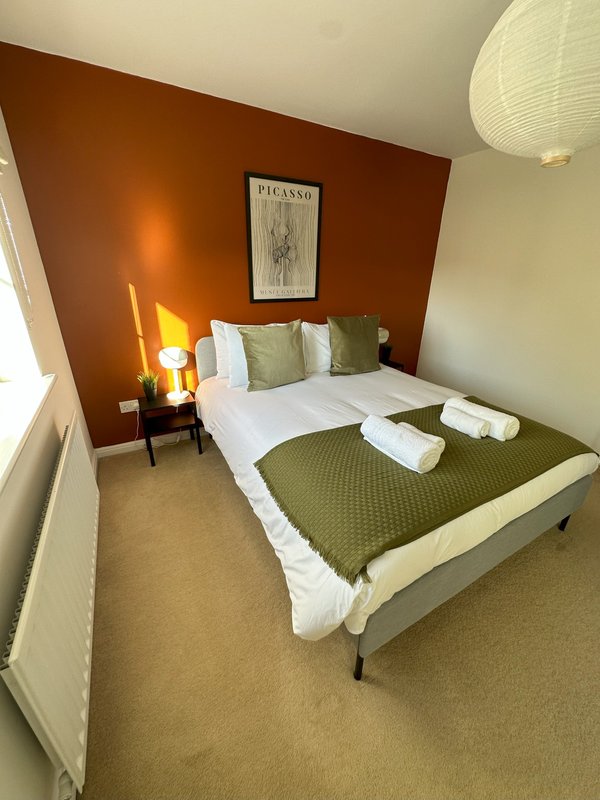 Bedroom with double bed, olive green bedding, framed artwork, and warm terracotta accent wall.