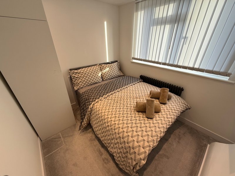 Small bedroom with double bed, patterned bedding, wooden blocks, and vertical blinds