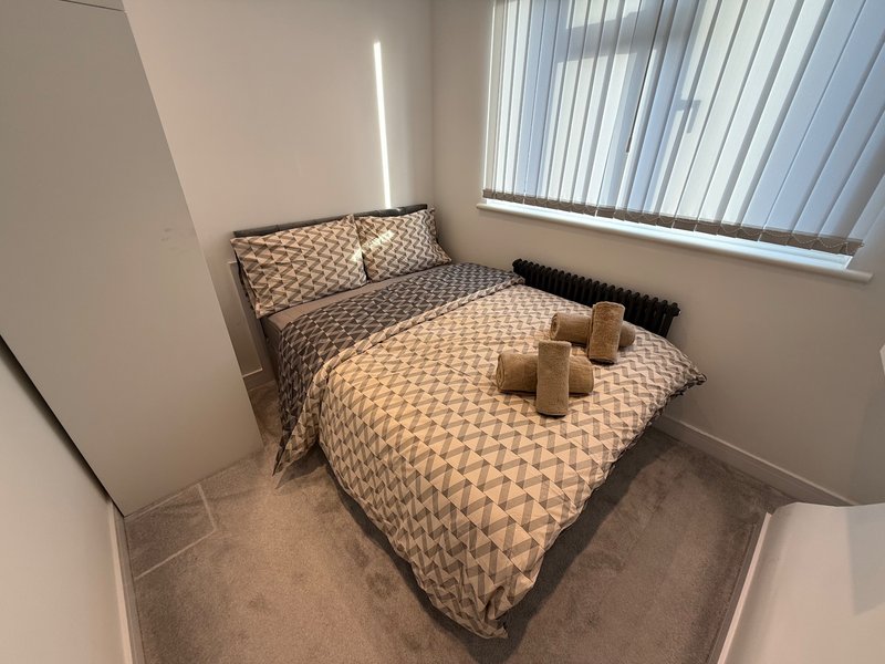 Minimalist bedroom with double bed, geometric patterned bedding, wooden candles, and bright window